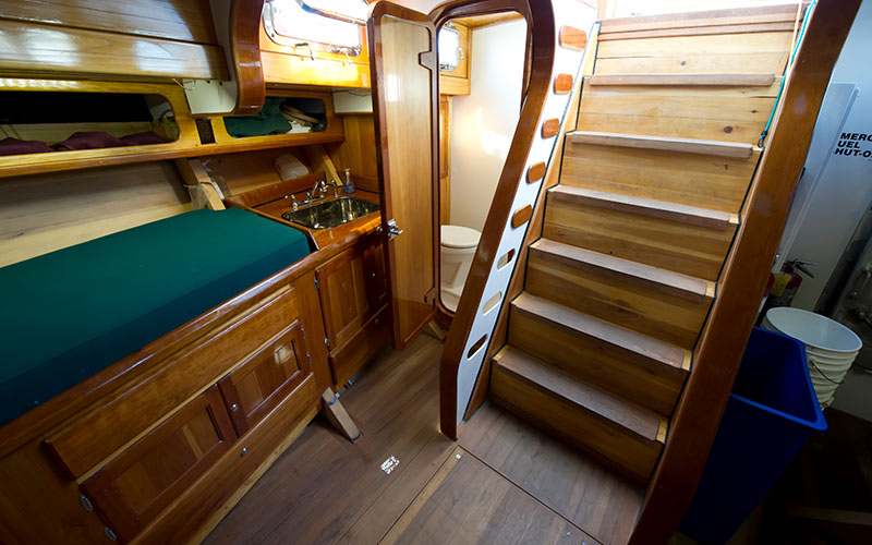 a lower deck view of the schooner america 2.0, with stairs to the deck as well as a small kitchen and bathroom