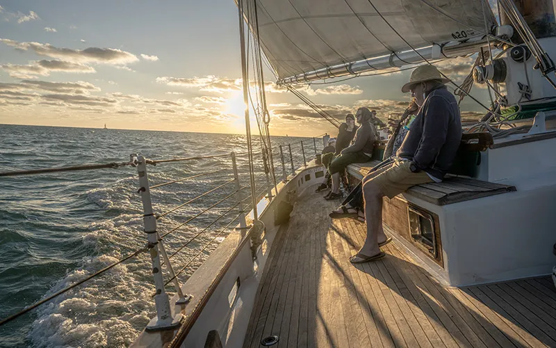 Guests sitting on the decks of Schooner America 2.0 with the sun setting in the background in Key West